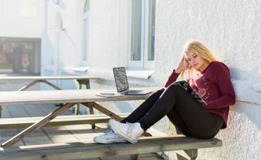 Ung jente sitter på benk og leser.
