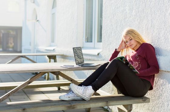 Ung jente sitter på benk og leser.